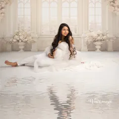 A serene and angelic portrait. The mother-to-be is seated in a heavenly white setting, with the water reflection adding a layer of dream-like calm to the image.