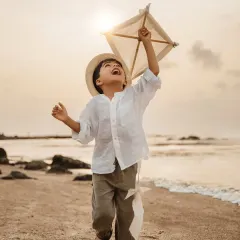 A young boy joyfully runs along the beach at sunset, flying a kite. This image captures the pure, carefree spirit of childhood, perfect for a milestone birthday or a kids outdoor photoshoot.