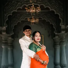 A classic portrait of an expecting couple in traditional attire. The photo is taken against a grand, carved archway, giving it a royal and timeless feel.
