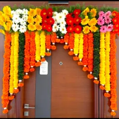 A simple front door flower decoration in Indian style. The door is adorned with hanging garlands of marigolds and a top border of colorful gerberas.