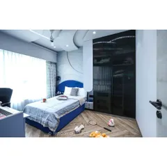 A modern classic bedroom for a teenager. The deep blue bed, smoked glass wardrobe, and curved false ceiling create a sophisticated and cool space that reflects her personality.