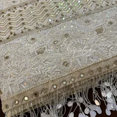 A detail shot of the saree's border and pallu, showing the intricate combination of Chikankari, mirrorwork, and shimmering sequins, complete with delicate tassels.