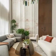A closer look at the seating arrangement in the Kolkata living room. We used a mix of curved sofas in white and grey to soften the space, centered around a smoked glass coffee table. The handcrafted marble wall serves as a stunning backdrop.