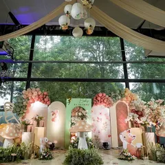 A wider view of the enchanted garden stage, showing the full scope of the decor against the venue's large glass windows. The setup included a white picket fence and glowing butterfly accents to complete the fairytale look.