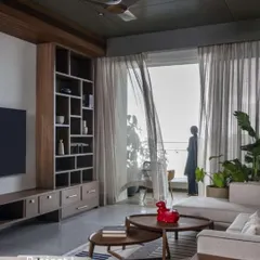 A glimpse into 'Project I' in Mahalakshmi, Mumbai. The living room is designed to feel grounded and authentic, with a custom wooden bookshelf, comfortable seating, and sheer curtains that filter the city light, creating a soft, pleasant atmosphere.