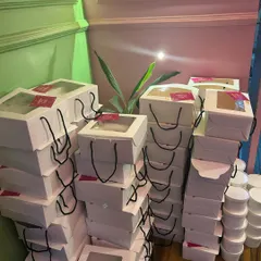 Stacks of my birthday boxes ready for delivery. Each box is a complete party meal, featuring a custom menu with items like Cheese Korean Buns, Pizza Samosas, and a Chinese Bowl. I handle bulk orders for parties of any size.