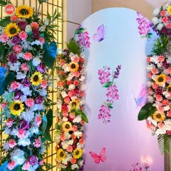 A close-up of the floral work from our pastel butterfly-themed Haldi. A dense arrangement of sunflowers, roses, and carnations in shades of pink, white, and yellow creates a lush texture against the dreamy, illustrated backdrop.