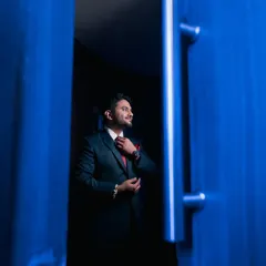 Suit up! A creative shot of the groom adjusting his tie, framed by a bold blue doorway.