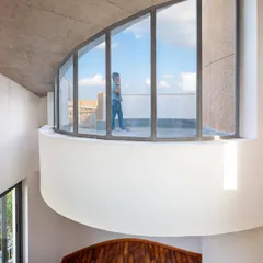 A curved balcony with floor-to-ceiling glass offers an expansive view, connecting the inhabitants with the sky and the surrounding environment.