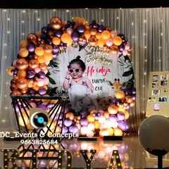 A trendy first birthday setup with a circular backdrop featuring a photo of the birthday girl. The organic balloon arch in metallic tones and marquee letters create a modern and stylish look.
