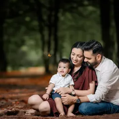 A candid family moment captured during an outdoor session in a wooded area. The warm, moody edit enhances the feeling of closeness and affection as the family sits together on the ground.