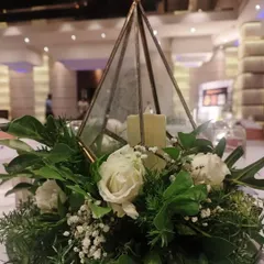 This elegant centerpiece was designed for a corporate dinner. A glass terrarium with candles is surrounded by a lush arrangement of white roses and fresh greenery, creating a sophisticated look.