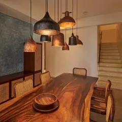 The dining area in the Magnolia Residence features a live-edge wooden table and custom-hammered copper pendant lights. The space is grounded by a blue accent wall, creating an intimate atmosphere for family gatherings.