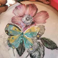 A student carefully adds detail to a butterfly and flower design during a fabric painting class. We use embroidery hoops to hold the fabric taut, allowing for precise and detailed work.