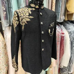 A showcase of regal craftsmanship. This black Jodhpuri suit features intricate gold hand embroidery on the shoulder and sleeve, creating a look of timeless elegance perfect for a groom or a grand event.