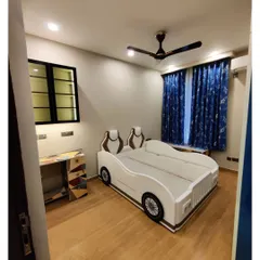 Another view of the custom car bed, showing how it fits into the overall room design. The wooden flooring and blue curtains complement the fun centerpiece, creating a cohesive and exciting space for a child.