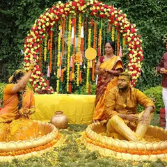 A fun-filled Haldi ceremony with the couple seated in large brass urlis, surrounded by a floral arch of red and yellow.