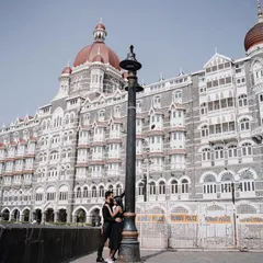 A long shot showing the couple in a quiet moment against the vast backdrop of the Taj hotel. This composition highlights the contrast between their intimacy and the grand scale of the city.