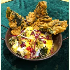 A sensational Palak Patta Chaat. Crispy spinach leaves are fried and topped with yogurt, chutneys, and pomegranate seeds for a perfect blend of spicy, sweet, and sour flavors.