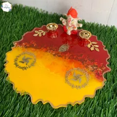 A festive pooja platter in auspicious shades of red and yellow, featuring swastika symbols and holders for diyas or kumkum.