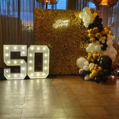 I make milestone birthdays like a 50th truly shine. This setup features a dazzling gold sequin shimmer wall, a custom "Happy Birthday" neon sign, and large, bright light-up marquee numbers that create the perfect photo opportunity.