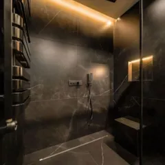 A luxurious, moody bathroom design with large-format black marble tiles. The walk-in shower features a built-in bench and subtle strip lighting to create a relaxing, spa-like experience.