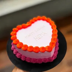 A simple and sweet heart-shaped birthday cake. The two-tone pink and orange buttercream border adds a vibrant touch.