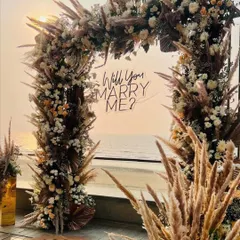 A closer look at the "Will you MARRY ME?" neon sign against the sunset. The sign is integrated into the pampas and floral arch, ensuring it’s a beautiful focal point for photos.