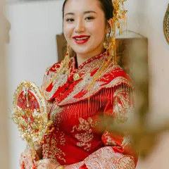 Our radiant bride dressed in a stunning traditional red and gold Chinese wedding outfit, complete with an ornate headdress and fan. We ensure every detail is authentic and respectful of the cultural heritage being celebrated.
