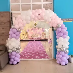 An impressive entrance to a banquet hall, with a large balloon arch in pastel purple, pink, and white, leading to a beautifully decorated venue.
