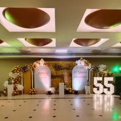 This view showcases the lighting and full scale of the 55th birthday setup in the event space. The combination of gold, white, and custom lighting creates a festive and elegant atmosphere.