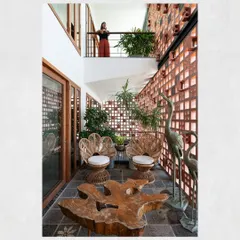 The alternating balconies at Kamala Residence create engaging visual connections between floors. This courtyard-like space is furnished with a live-edge table and peacock-style cane chairs, creating a private garden oasis.