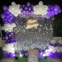 A purple and white balloon arch frames this silver shimmer wall, creating a vibrant and fun photo corner for a birthday celebration.