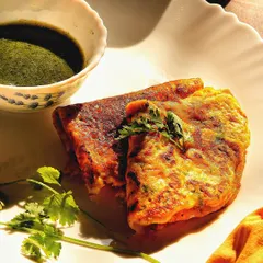 A healthy and delicious moong dal chilla (a savory Indian pancake) served with green chutney. The bright, natural light highlights the fresh ingredients and makes it look incredibly appetizing.