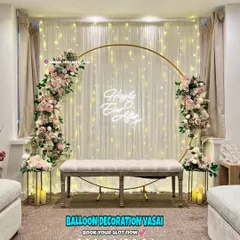For an elegant engagement or anniversary party, I can create a beautiful photo backdrop like this one. It features a large golden ring decorated with soft pink and white floral arrangements, set against a backdrop of twinkling fairy lights and a "Happily Ever After" neon sign.