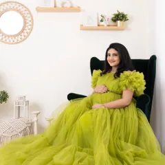 A solo portrait of a beautiful mom-to-be, seated gracefully in a green armchair and wearing a flowing lime-green gown. This studio shot highlights the serene glow of pregnancy.