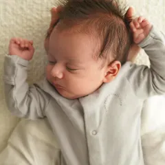 An overhead shot of a sleeping newborn stretching their arms. The baby's spiky hair and cute expression are the focus, showing the natural moments I capture at home.