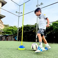 This player is working on agility and ball mastery around a training pole, a drill that enhances coordination and the ability to maneuver in tight spaces.