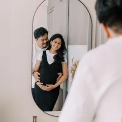 A creative reflection shot capturing the couple's embrace in the mirror. This perspective adds a layer of intimacy and artistry to the home maternity session, showing the moment from a different point of view.