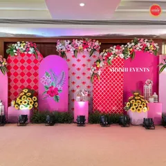 This stage backdrop plays with shades of pink, patterns, and floral art. Arched panels with geometric and botanical prints are layered to create depth, while arrangements of sunflowers and other blooms add a fresh, organic element.