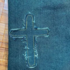 A close-up of the frayed cross patch detail. Notice the precise stitching that secures the patch while allowing for a rugged, textured edge.