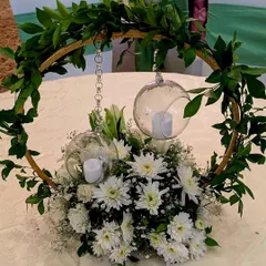 A modern and minimalist centerpiece, featuring a golden hoop with hanging glass orbs and candles, set within a bed of white chrysanthemums and baby's breath.