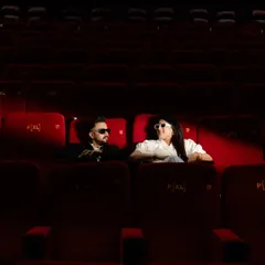 A cool, cinematic shot of a couple in an empty movie theatre. The dramatic red lighting and their stylish sunglasses give this pre-wedding photo a bold, movie-star vibe.