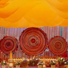 The stage backdrop for the equestrian Haldi, featuring large, circular woven mats in shades of red and orange, creating a rustic and textural focal point.