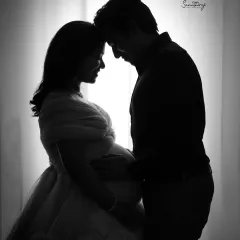 A classic backlit silhouette of a couple against a bright window. The dramatic contrast highlights their forms and the intimate moment they share, creating a timeless black and white image.