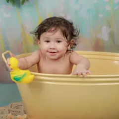 This happy baby plays with a rubber duck during his bath time session. We use classic, fun props to encourage natural smiles and playful interactions.
