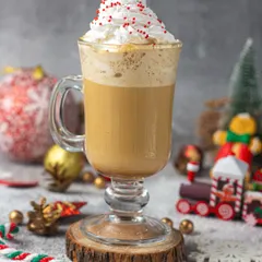 A cozy shot of a Christmas coffee drink topped with whipped cream and sprinkles, set against a festive, snowy background.