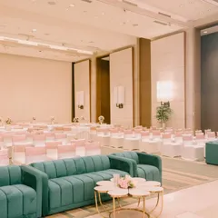 A sophisticated indoor setup for an engagement. The hall is filled with beautifully arranged seating, and the stage is set with modern teal sofas for a pop of color.