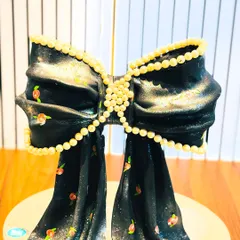 An elegant and glamorous cake sculpted into a large, shimmering black bow. The design features a delicate floral print and edible pearl details, giving it the look of high-fashion fabric.