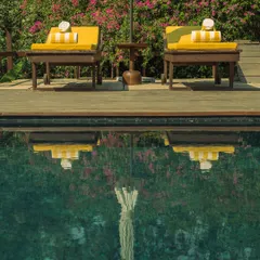 The still water of the pool creates a perfect reflection of the poolside loungers and the vibrant bougainvillea.